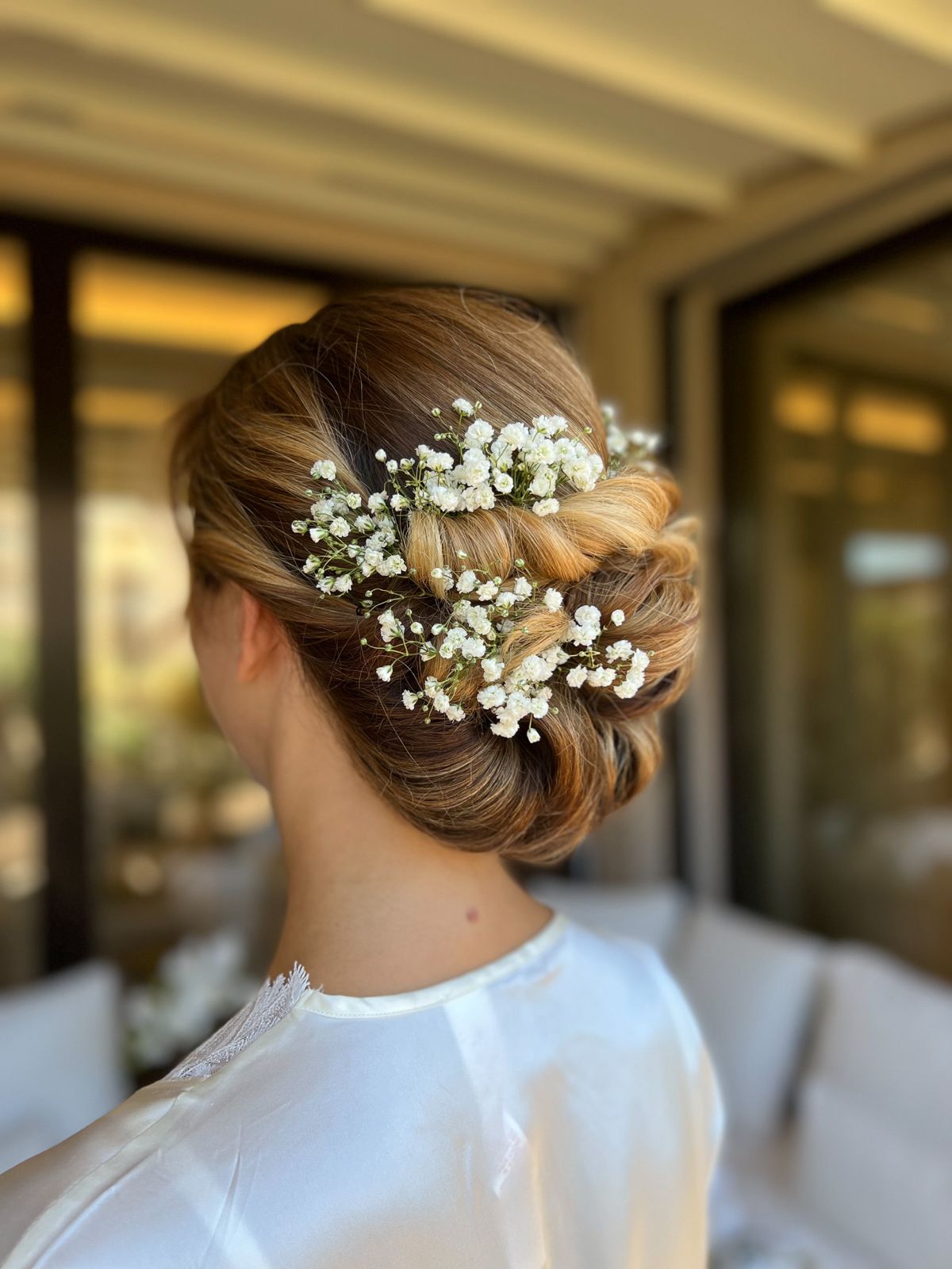 Chignon con gypsophila su capelli miele, sposa in vestaglia di seta