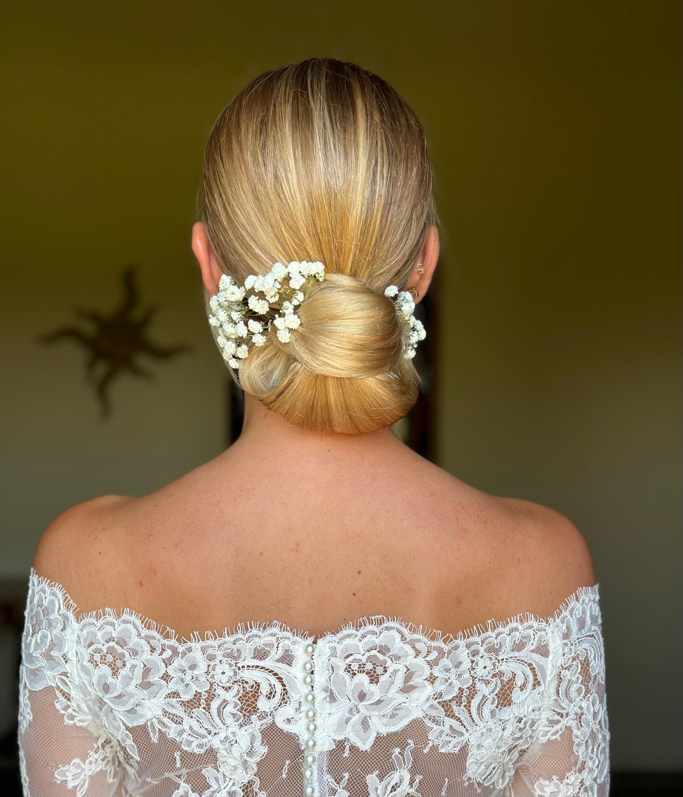 Sposa di spalle con chignon basso liscio e fiori di gypsophila